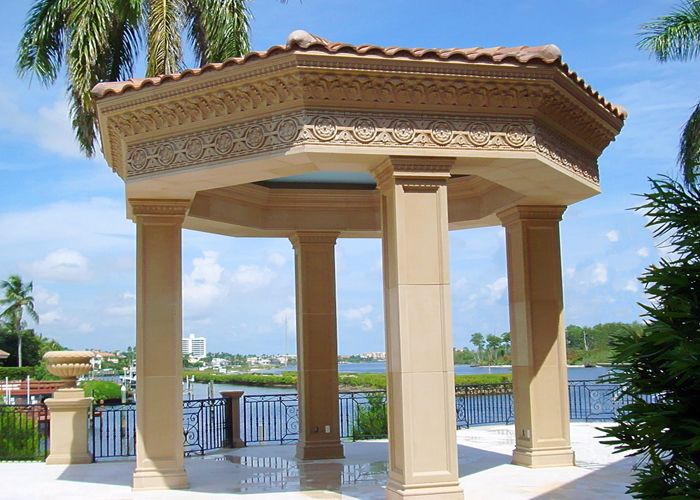 Ornate cast stone gazebo with carved cornice frieze and columns overlooking waterway